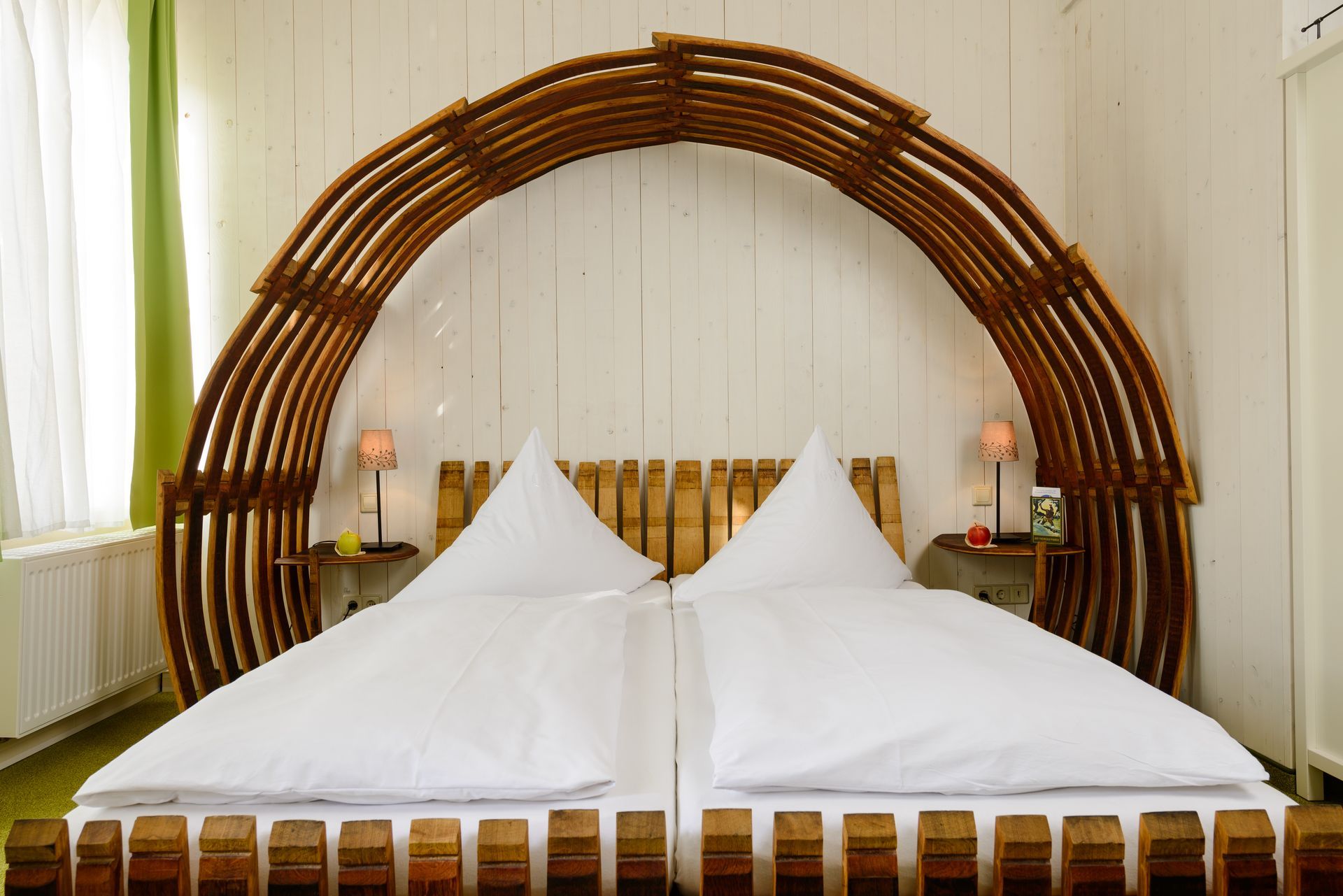 Bett mit einzigartigem, gewölbtem Holzkopfteil, zwei weiß bezogenen Kissen, kleinen Nachttischen mit Lampen.