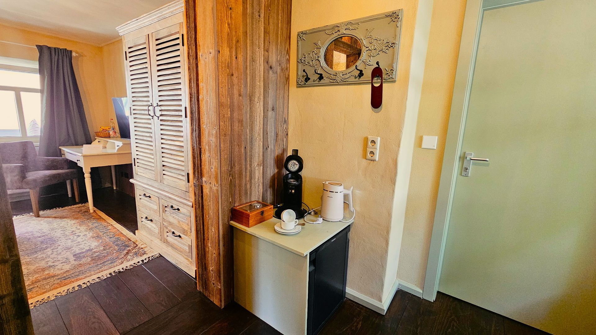 Schlafzimmerinterieur mit Kleiderschrank, Kaffeestation, Tür, Teppich, Schreibtisch und Fenster.