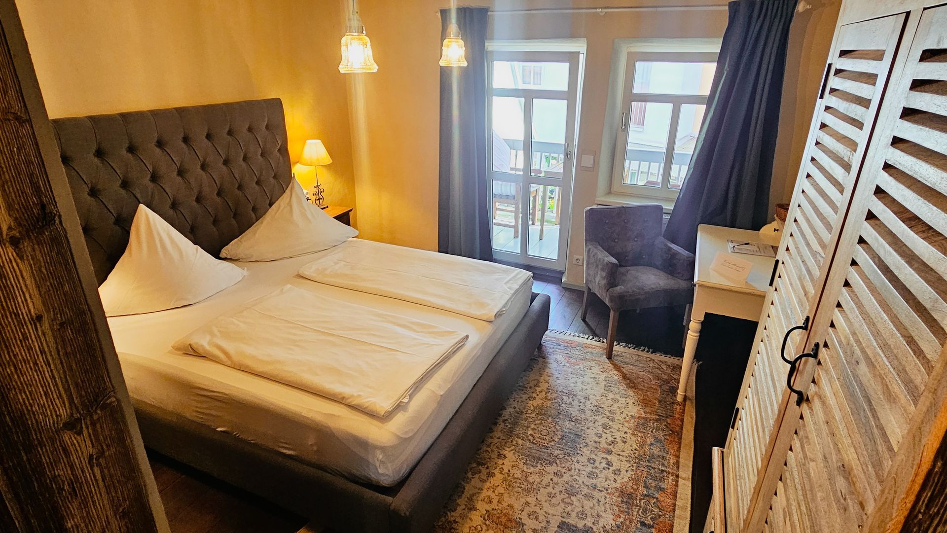 Schlafzimmer mit gestepptem Kopfteil, zwei weißen Betten, einem Fenster und einem Holzschrank.