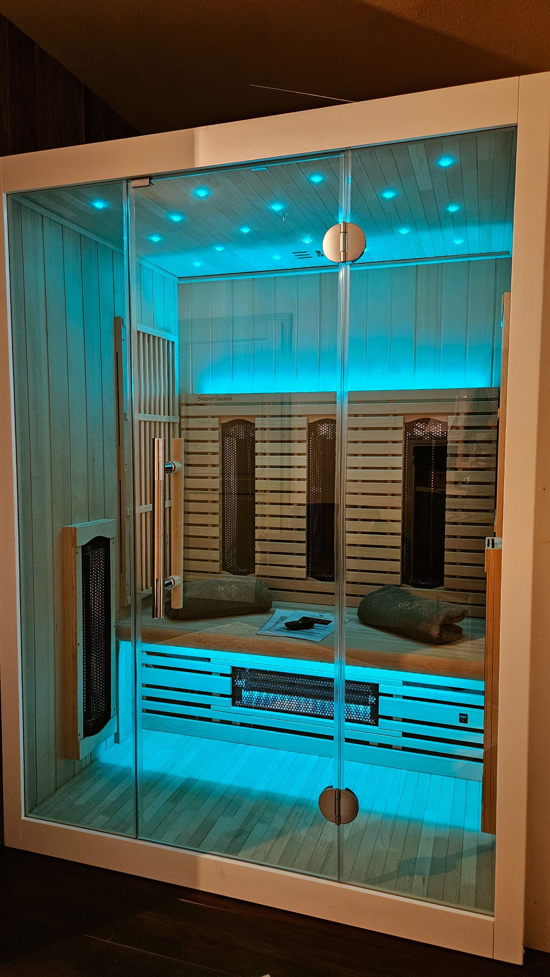 Moderne Sauna mit blauer LED-Beleuchtung, Holzinnenausstattung, Glastüren und digitalem Bedienfeld.