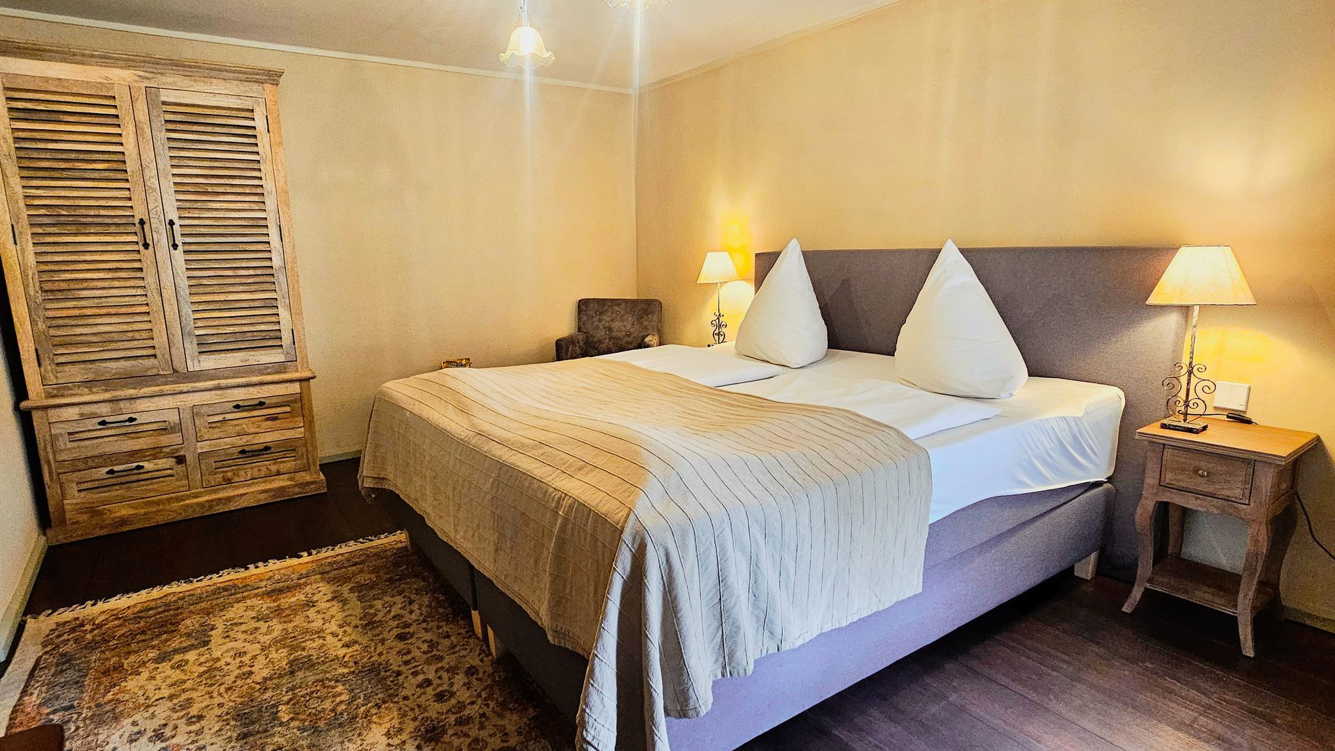 Schlafzimmer mit Kingsize-Bett, Lampen, Holzschrank und kleinem Teppich.