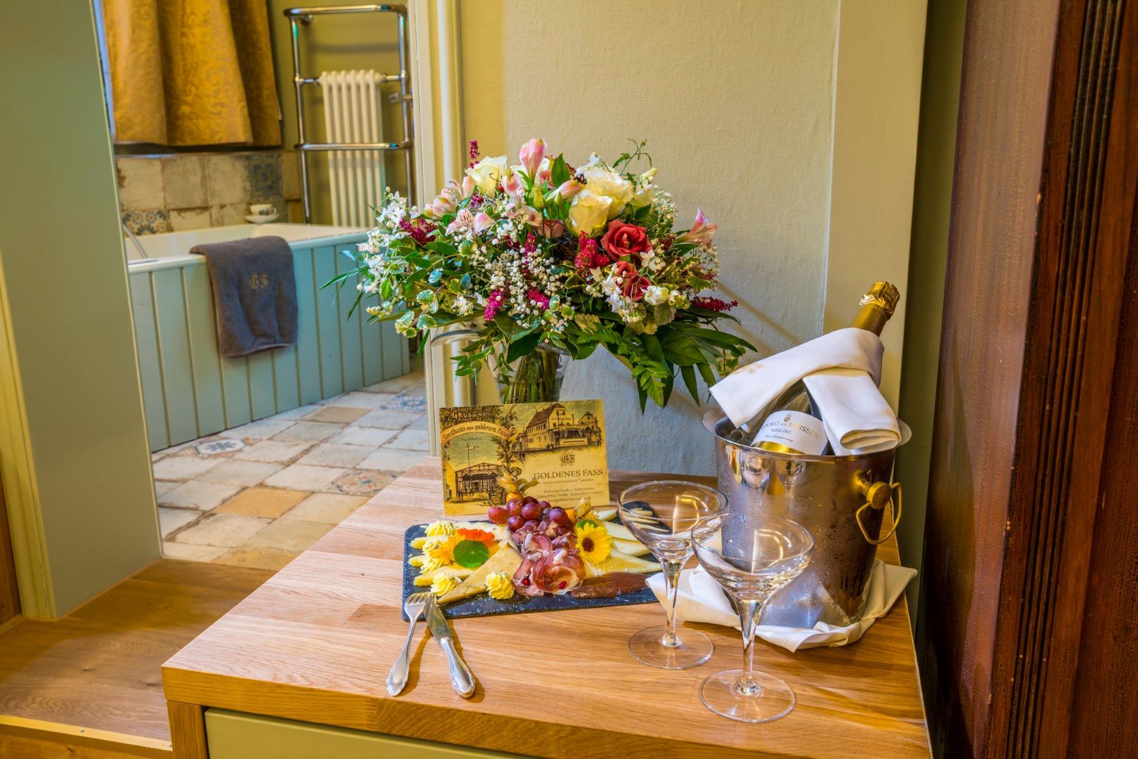 Ein Tisch mit einem Blumenstrauß, einer Wurstplatte und einem Champagnerkühler mit zwei Gläsern, vor einem Whirlpool.