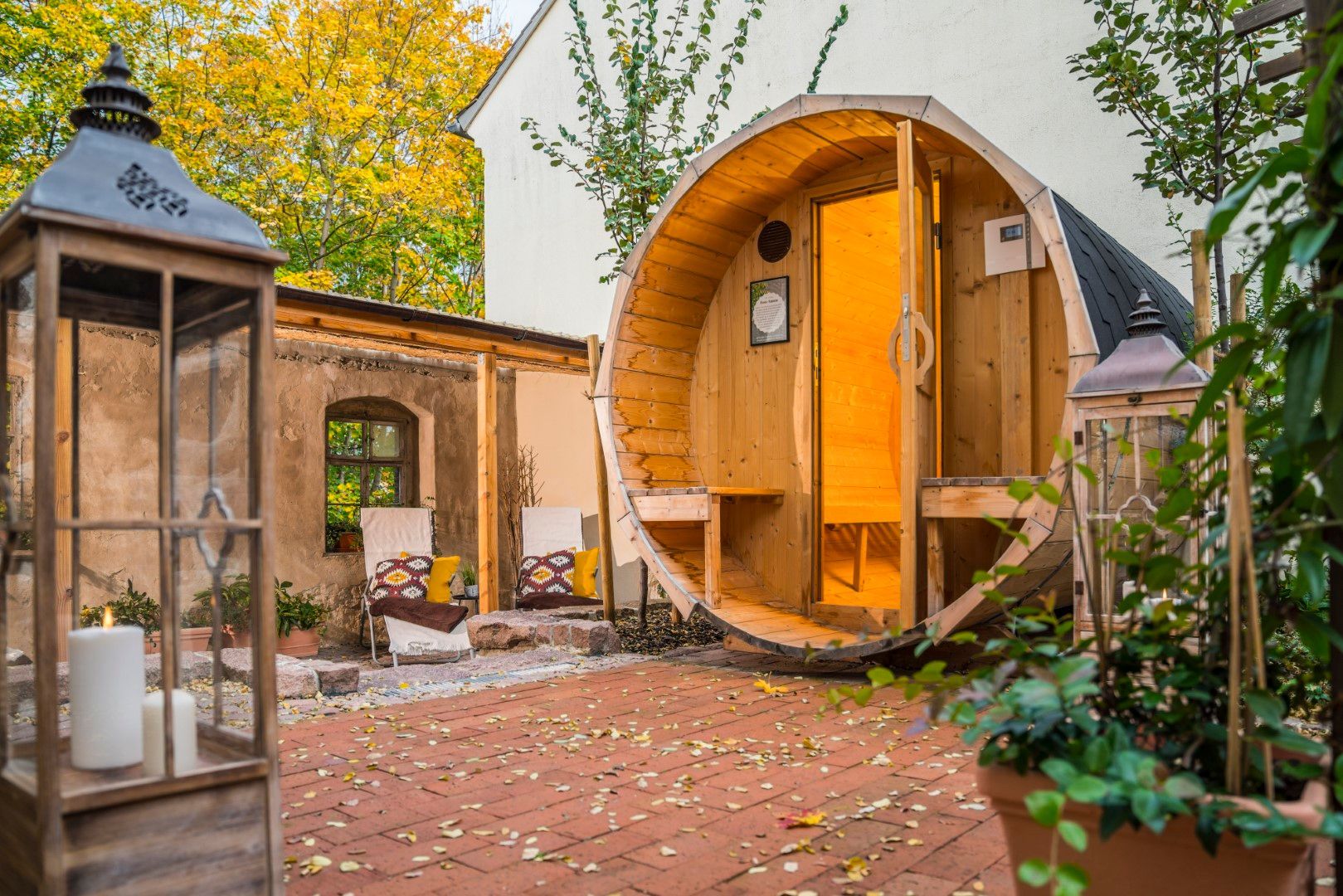 Sauna aus einem Holzfass, im Freien. Terrasse aus Ziegelsteinen, Laterne, Stühle und Pflanzen.