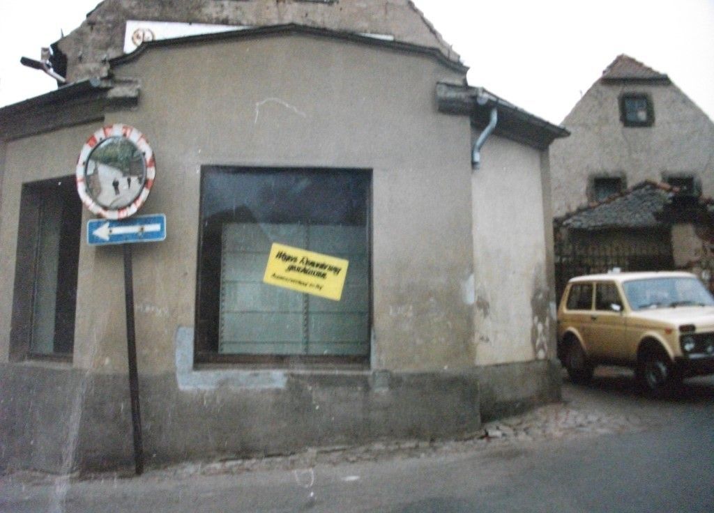 Eckgebäude mit Schild im Fenster, Straßenschild und einem gelben Auto.