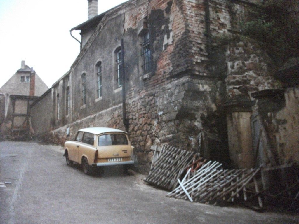 Ein verwittertes Gebäude mit einem geparkten Auto in einer schmalen Straße. Das Gebäude ist grau und braun.