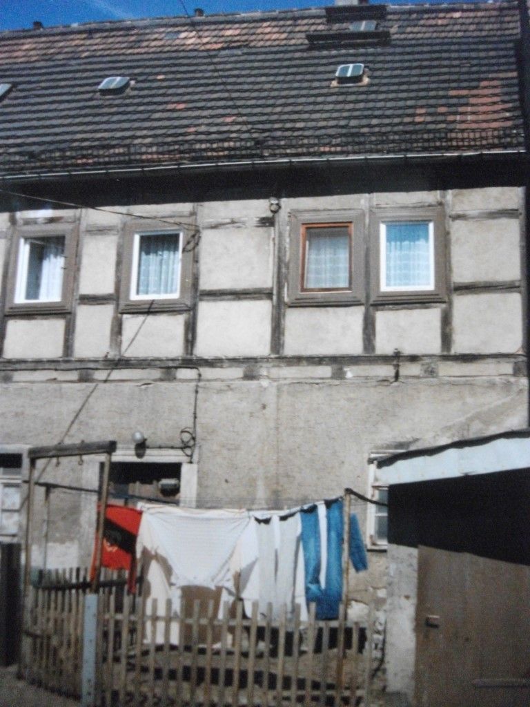 Zweistöckiges Gebäude mit Fachwerk-Obergeschoss, Wäscheleine im Vordergrund und Holzzaun.