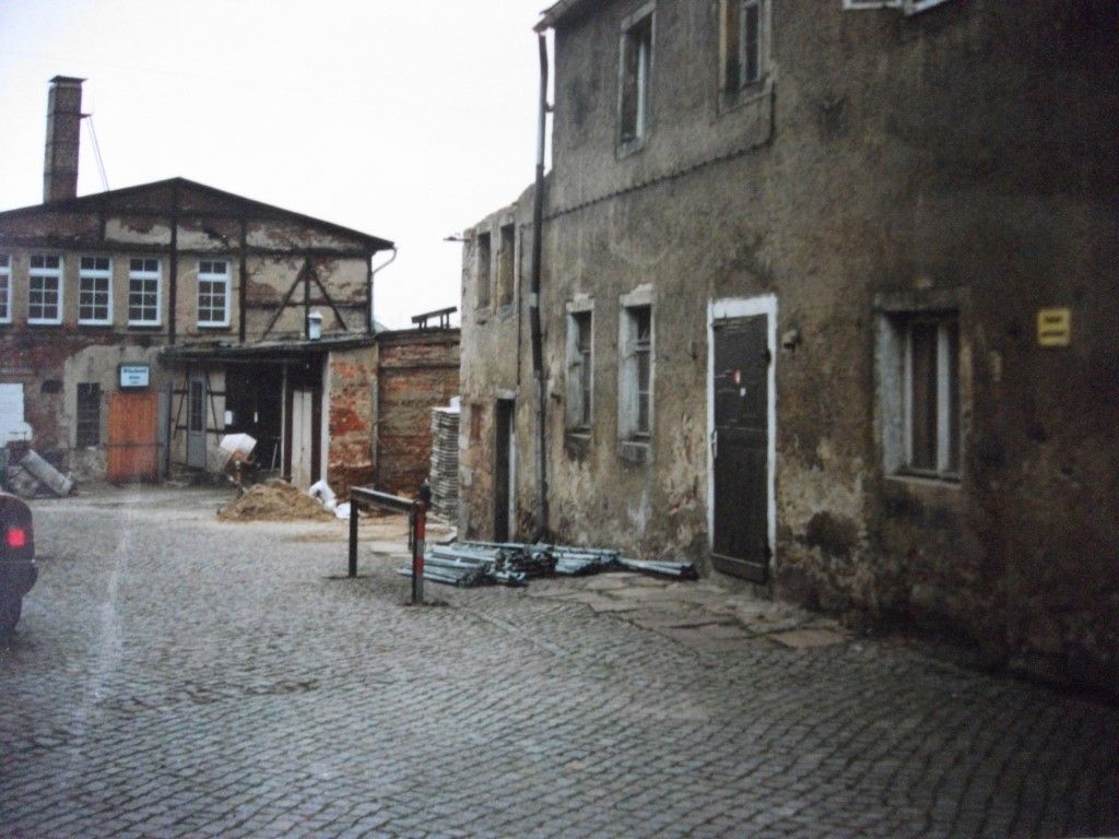 Kopfsteinpflasterhof mit verwitterten Gebäuden und einem Schornstein.