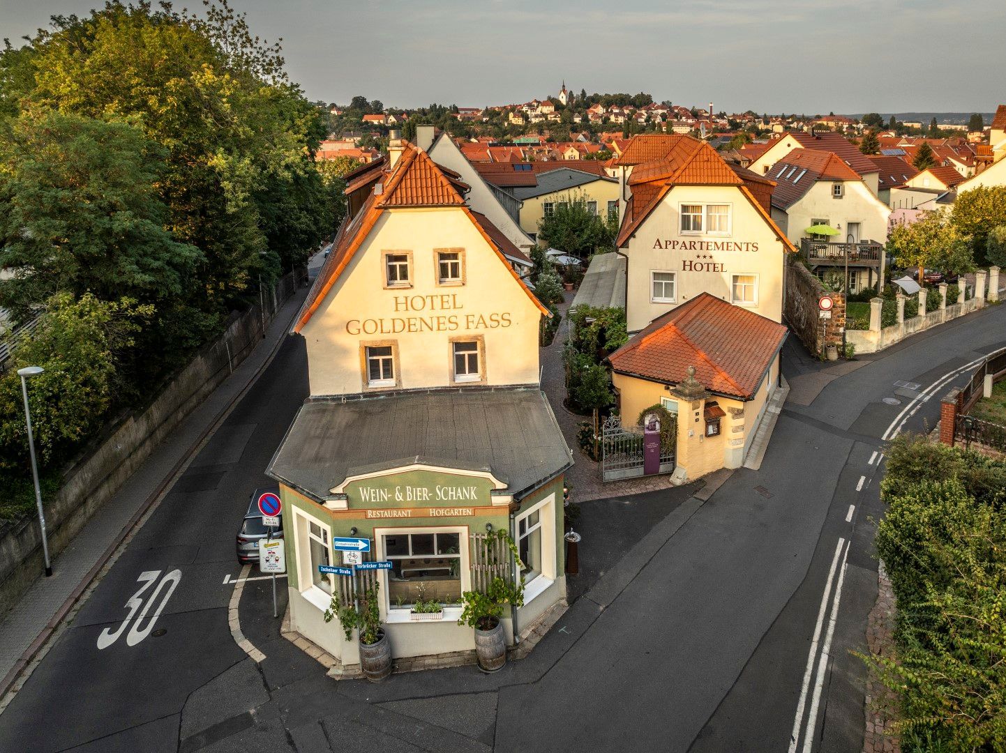 Eine Straßenecke in einer deutschen Stadt mit Gebäuden und einem Restaurant. Braune Ziegeldächer, Stuckwände und ein 30-Meilen-pro-Stunde-Schild.