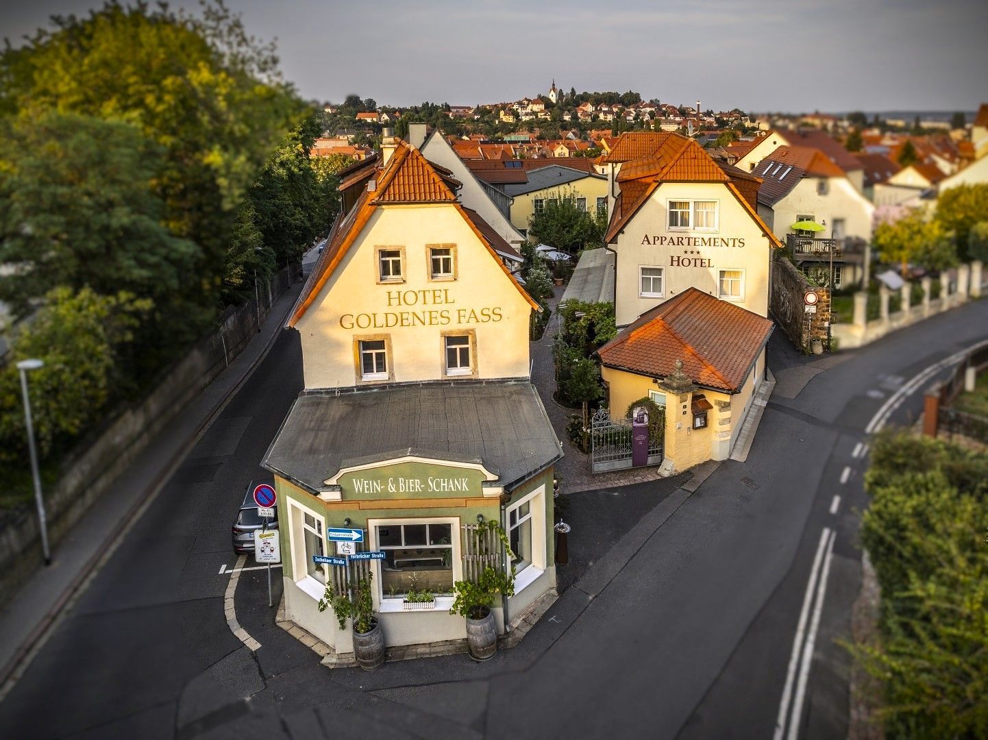 Hotelgebäude mit roten Ziegeldächern an einer Straßenecke, im Hintergrund die Stadt Meißen an der Elbe.
