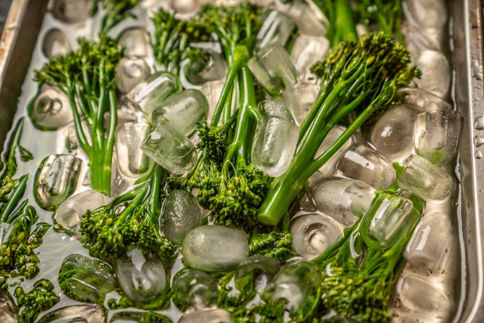 Brokkoli in einer Metallschale mit Eiswürfeln und Wasser, Blanchierprozess.
