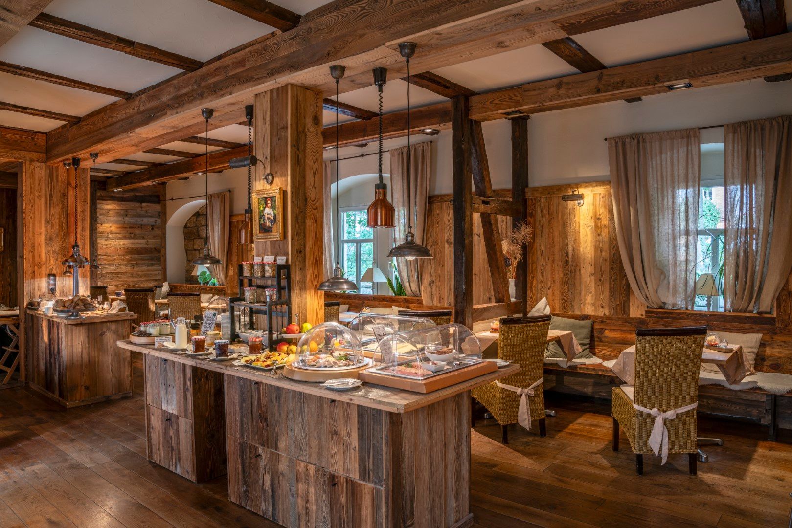 Frühstücksbuffet aus Holz in einem rustikalen Speisesaal mit Balkendecke, Speisenauslagen und Sitzgelegenheiten.