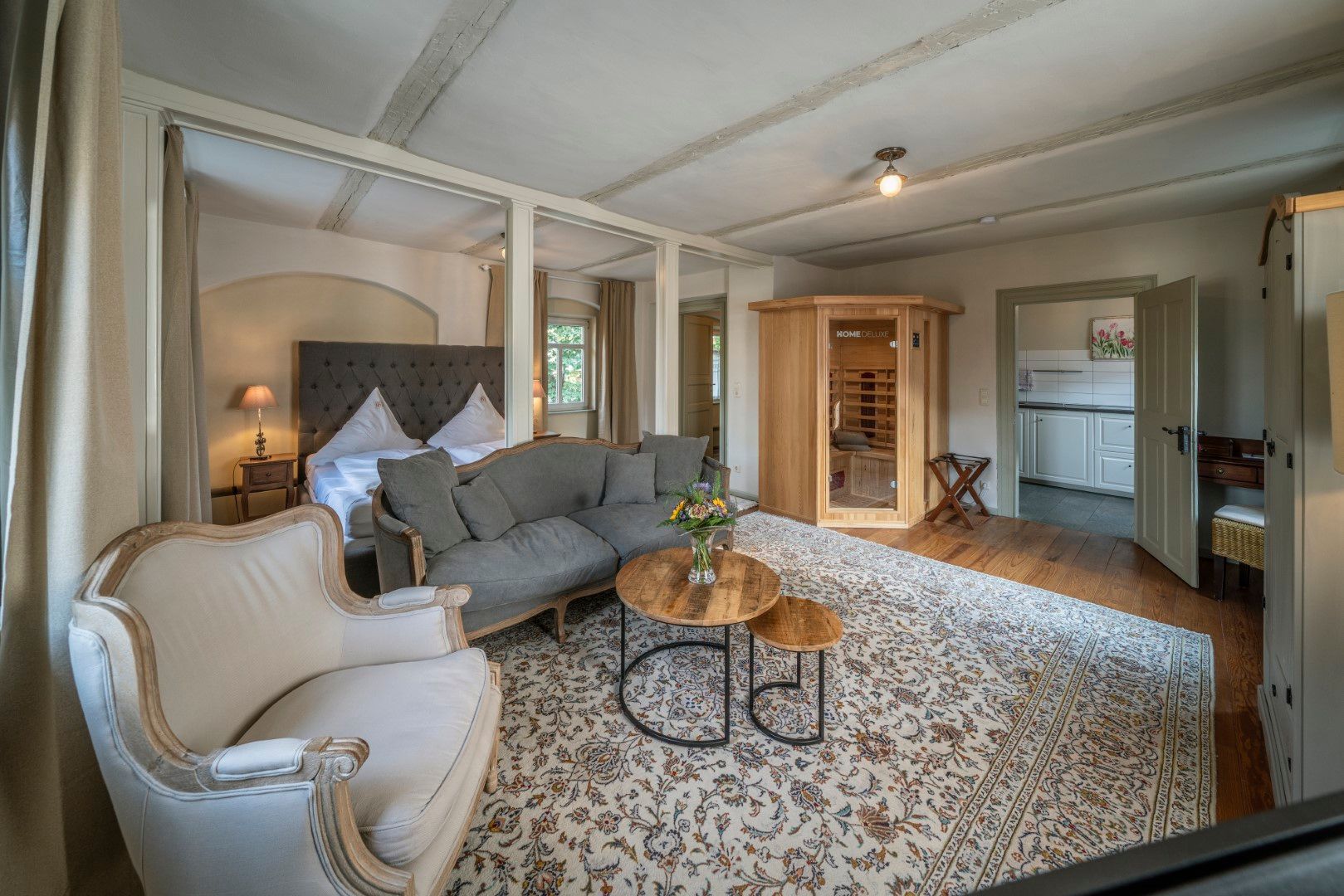 Elegantes Hotelzimmer mit Bett, Sofa, Sauna und gemustertem Teppich.