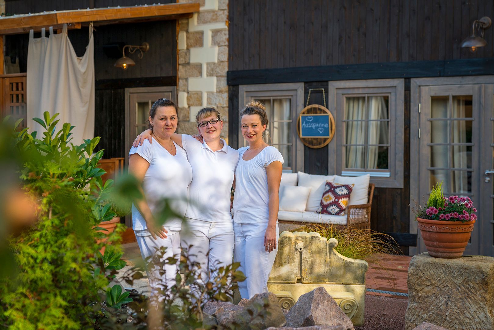 Drei Personen in Weiß, die im Freien in der Nähe eines Gebäudes mit Stein- und Holzelementen stehen.