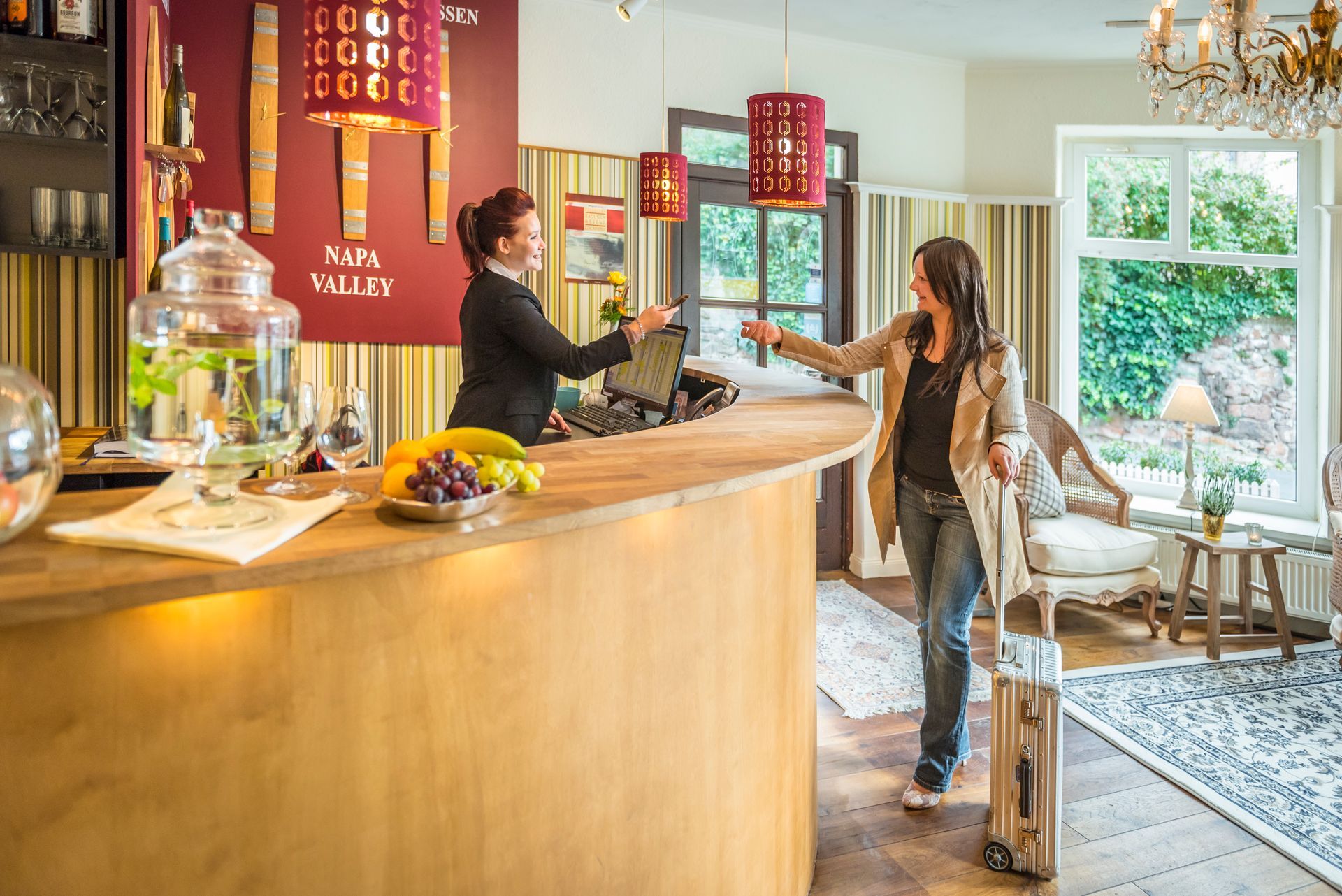 Eine Frau checkt an der Hotelrezeption ein. Theke mit Obst- und Getränkespender.