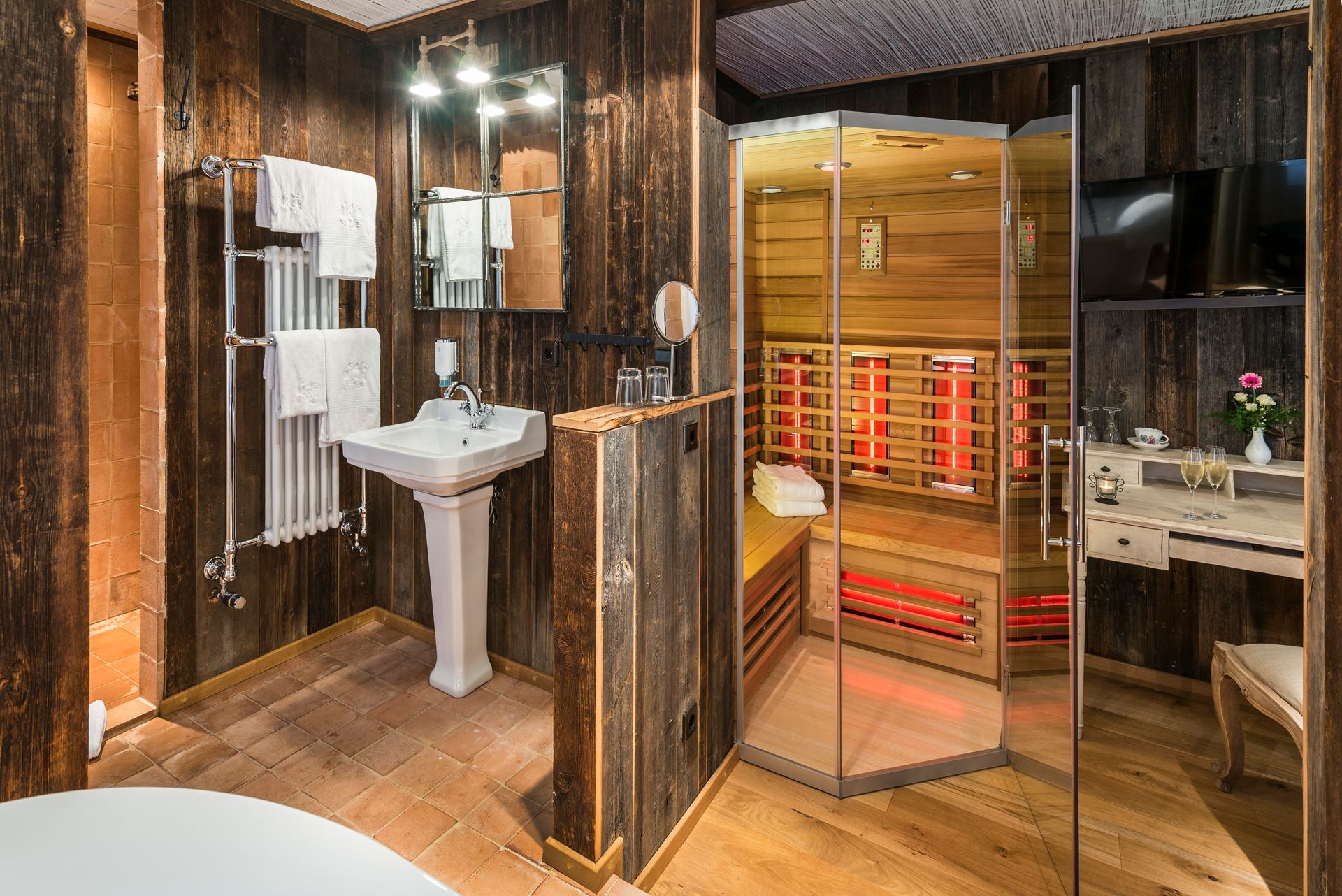 Badezimmer mit Holzvertäfelung, ausgestattet mit Waschbecken, Spiegel, Handtuchhalter und Sauna.