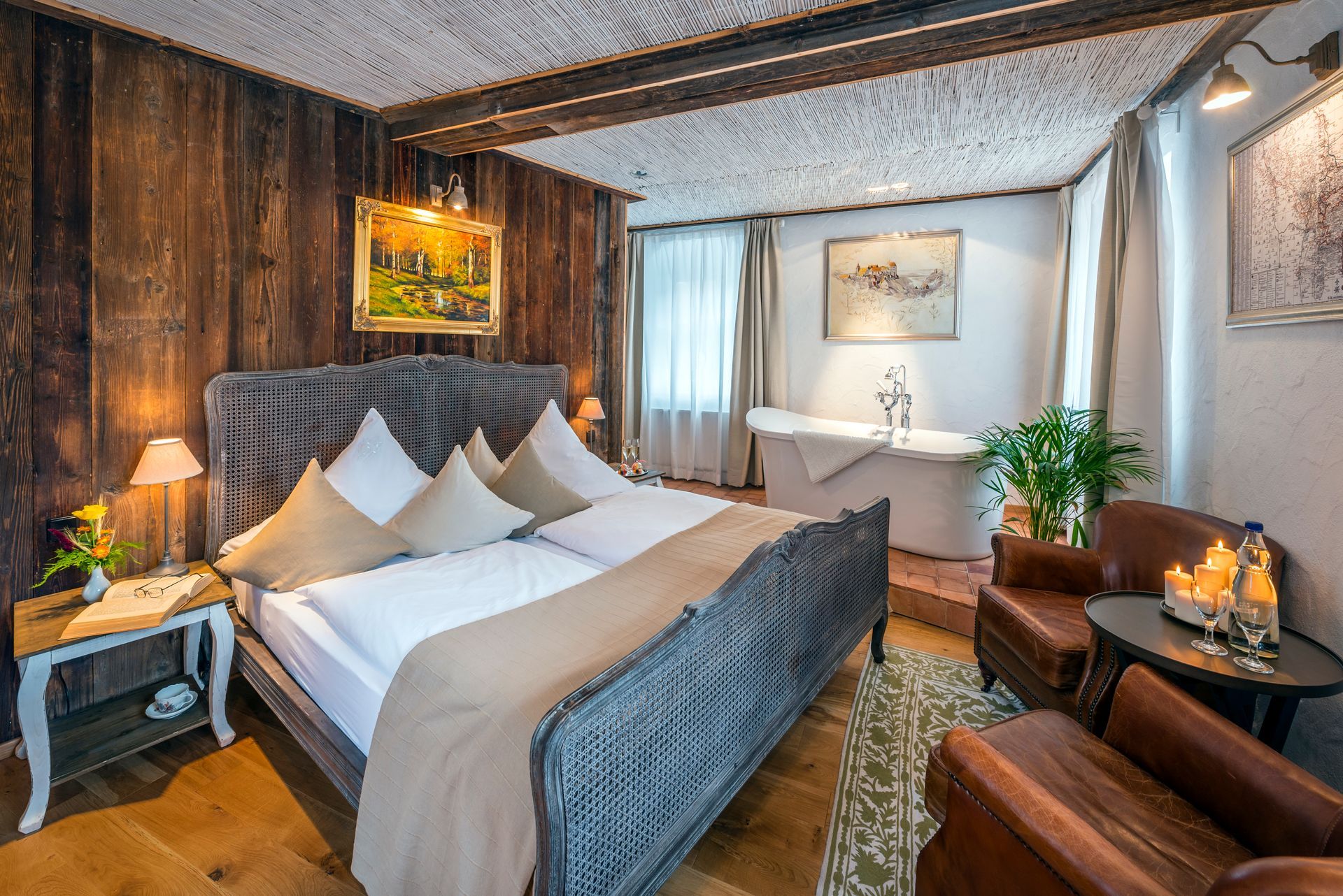 Gemütliches Schlafzimmer mit Korbbett, Holzwänden, einer weißen Badewanne und zwei Ledersesseln.