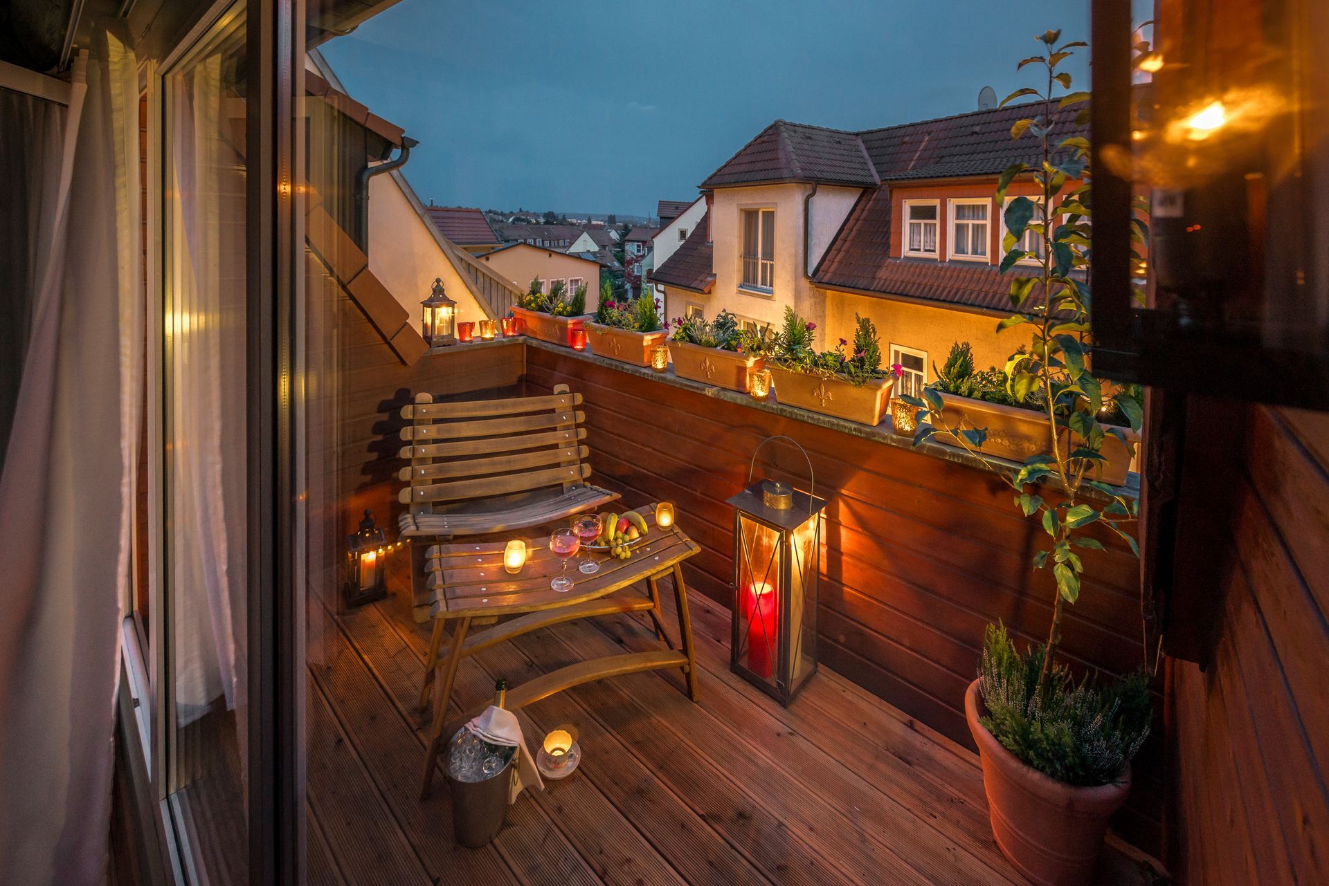Gemütlicher Balkon in der Abenddämmerung, Holzmöbel, Kerzen, Blick auf alte Gebäude.