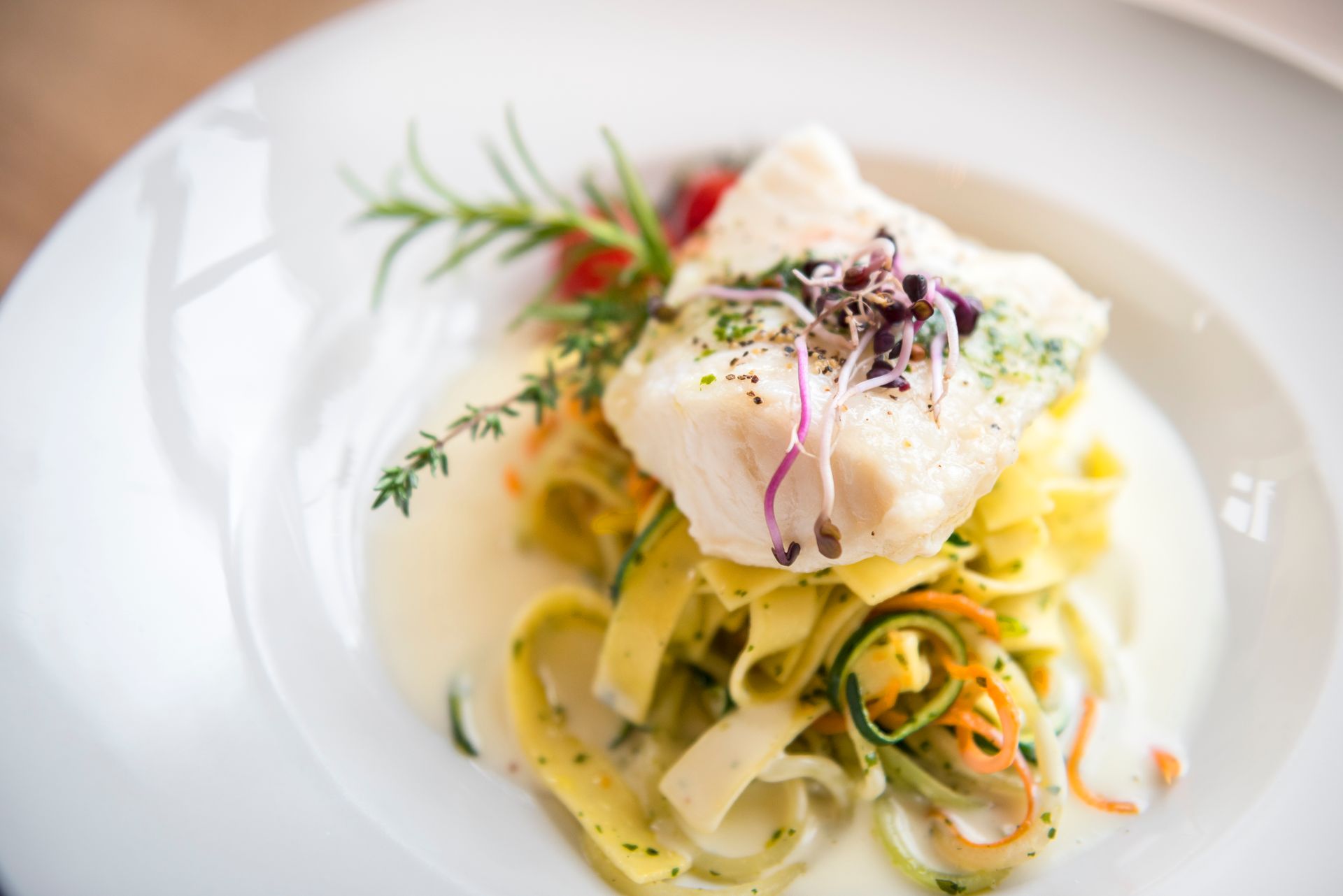 Weißfischfilet auf Pasta, mit Sauce und Garnitur auf einem weißen Teller.