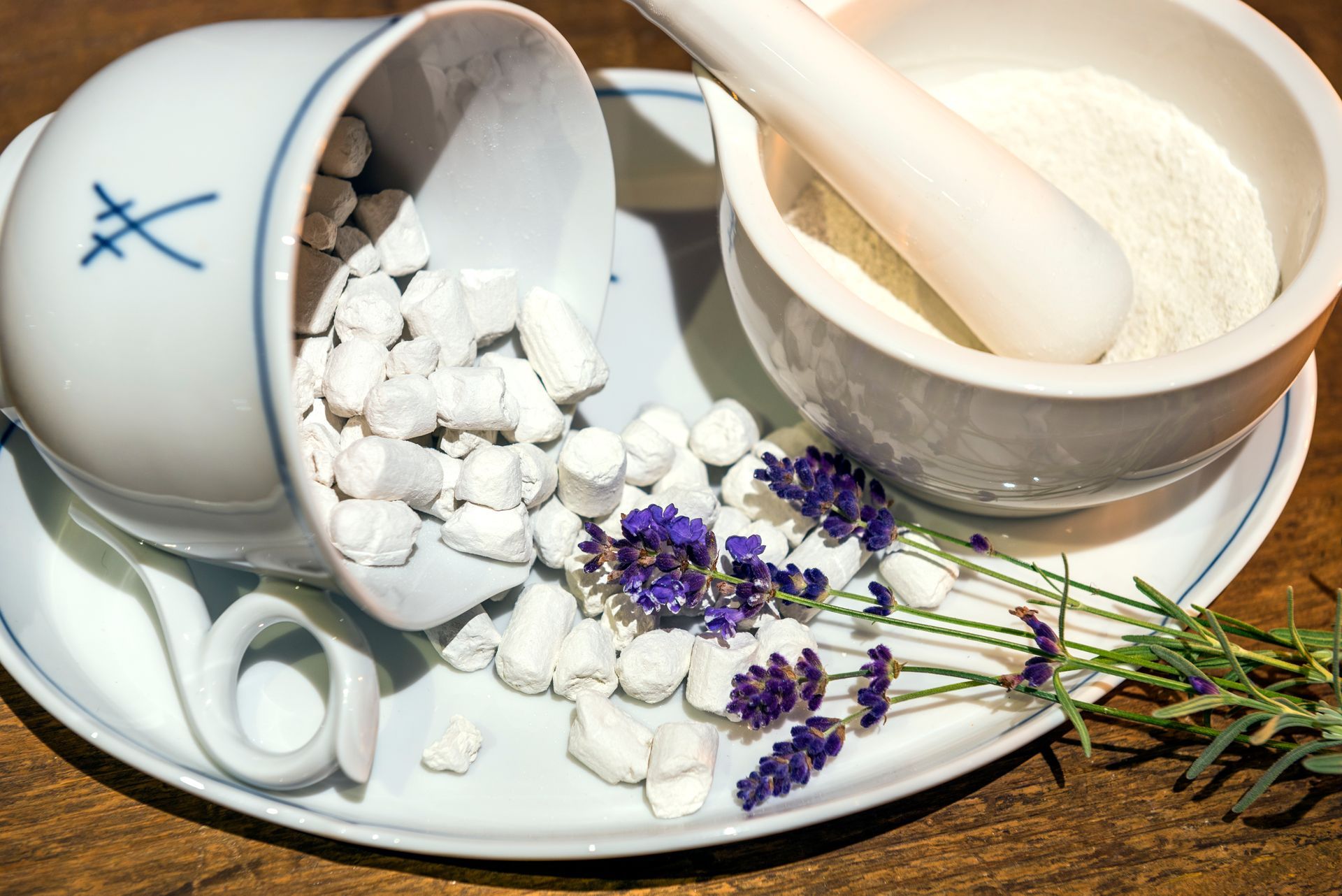 Weißer Keramikmörser und -becher mit verstreuten weißen Kügelchen und Lavendel auf einer Untertasse.