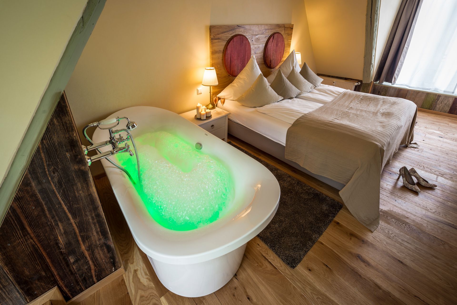 Ein Schlafzimmer mit freistehendem Whirlpool mit leuchtend grünem Schaum, angrenzend an ein Bett mit Bettwäsche und Kissen.