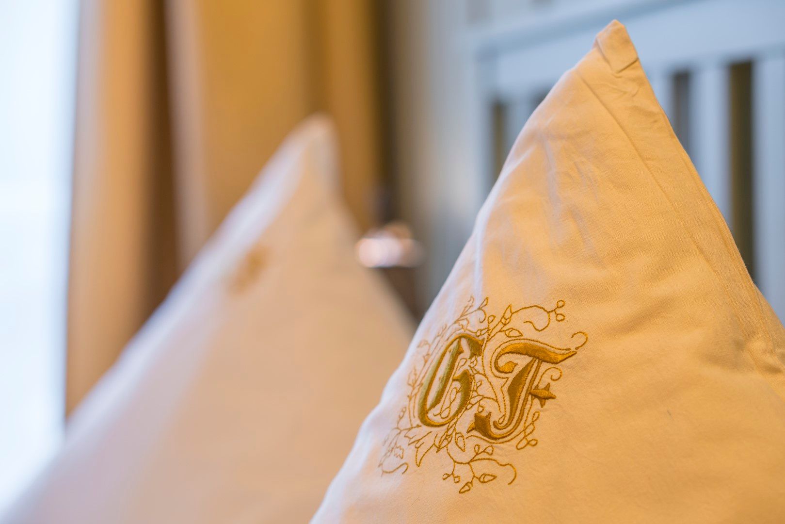 Zwei weiße Kissen mit goldgestickten Initialen „GF“.