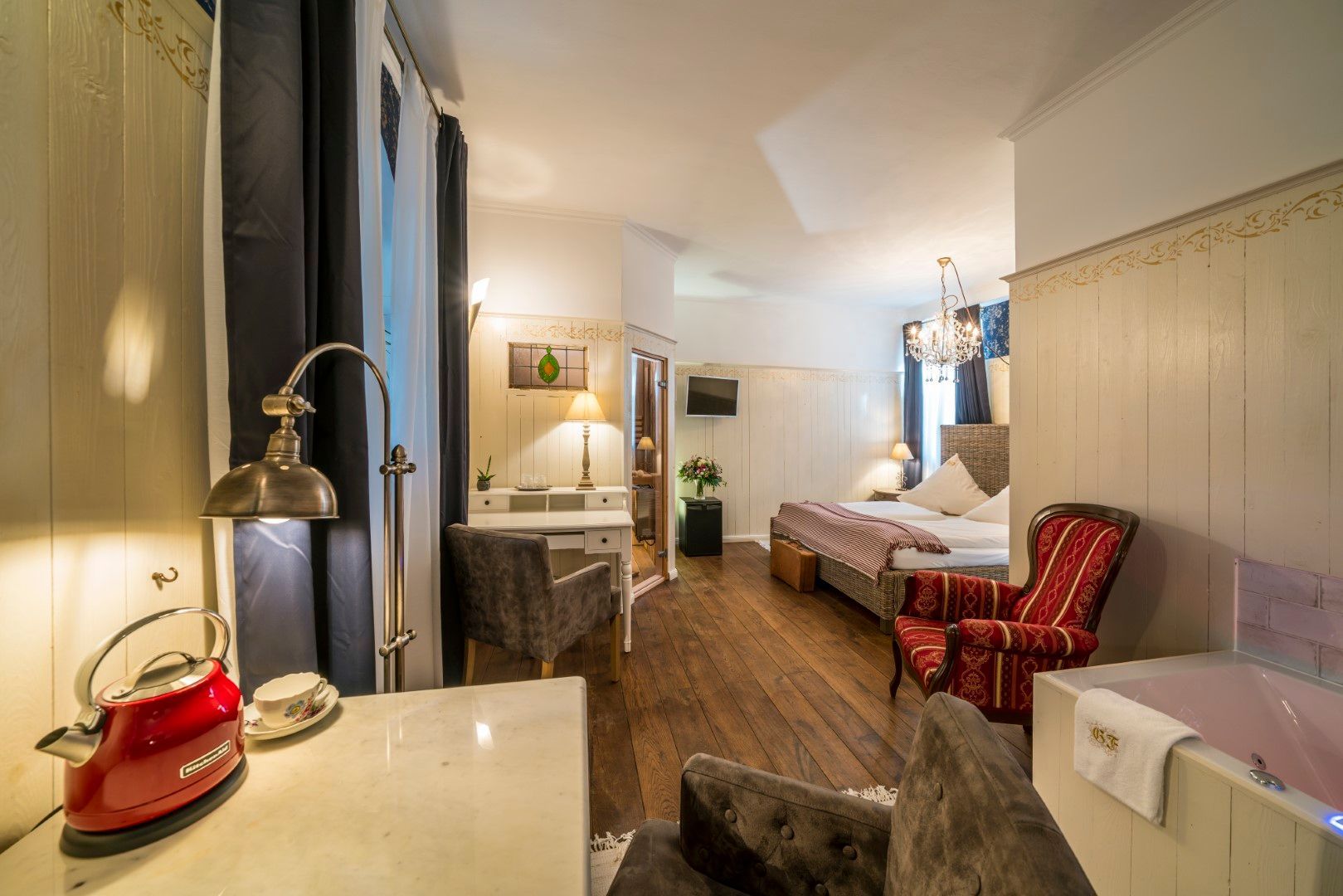 Gemütliches Hotelzimmer mit Bett, Schreibtisch und rotem Sessel, Whirlpool und Vintage-Dekor.