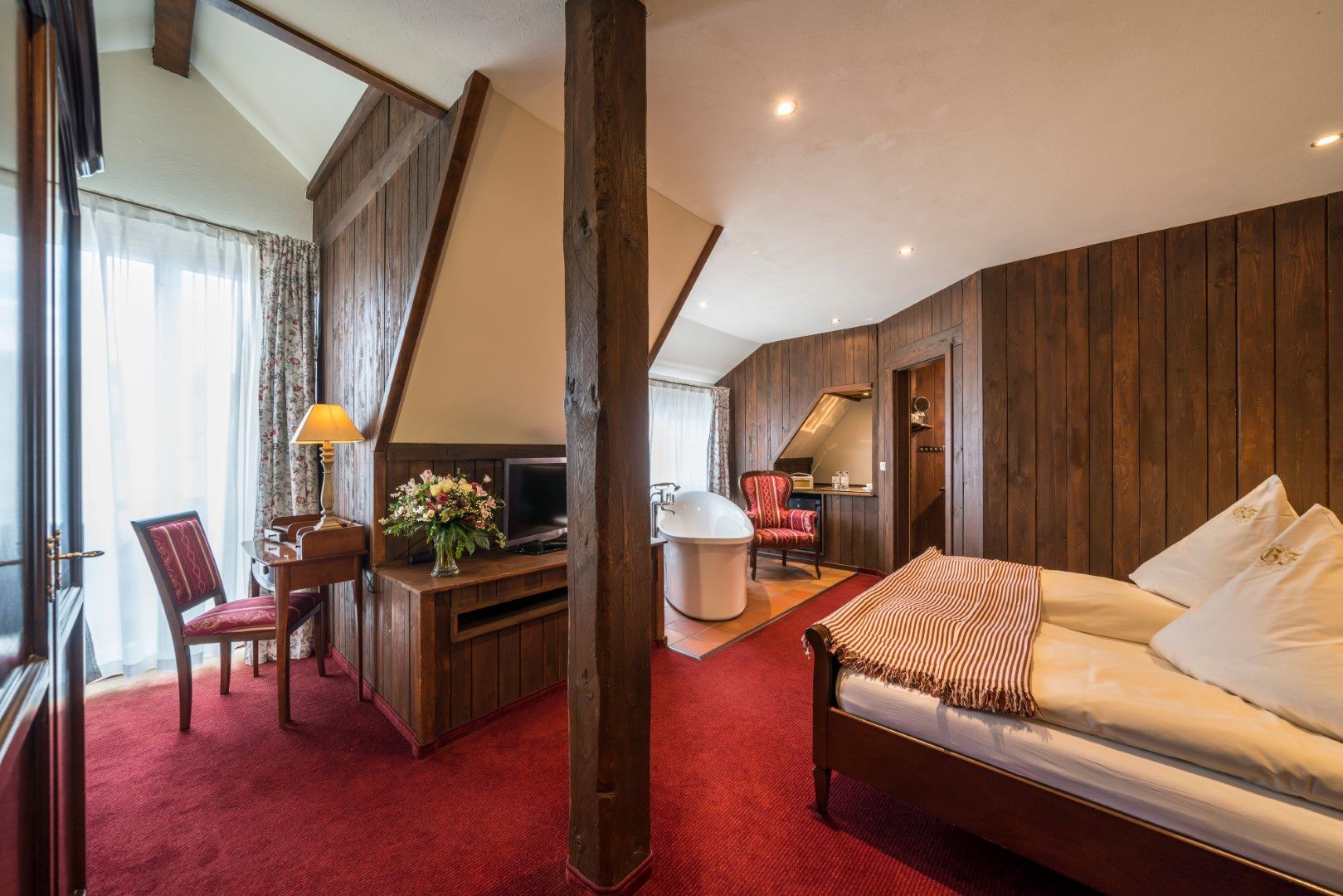 Hotelzimmer mit Holzwänden, rotem Teppich, Schreibtisch und Bett.