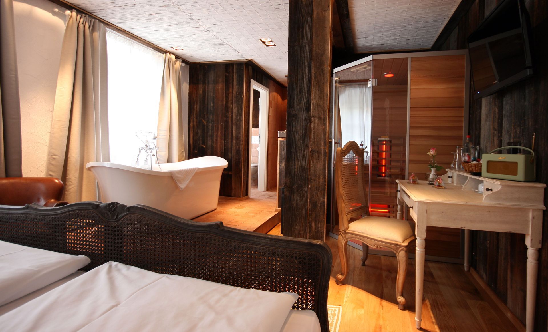 Hotelzimmer mit Badewanne in Fensternähe, Bett und einem Holzschrank mit Schreibtisch.