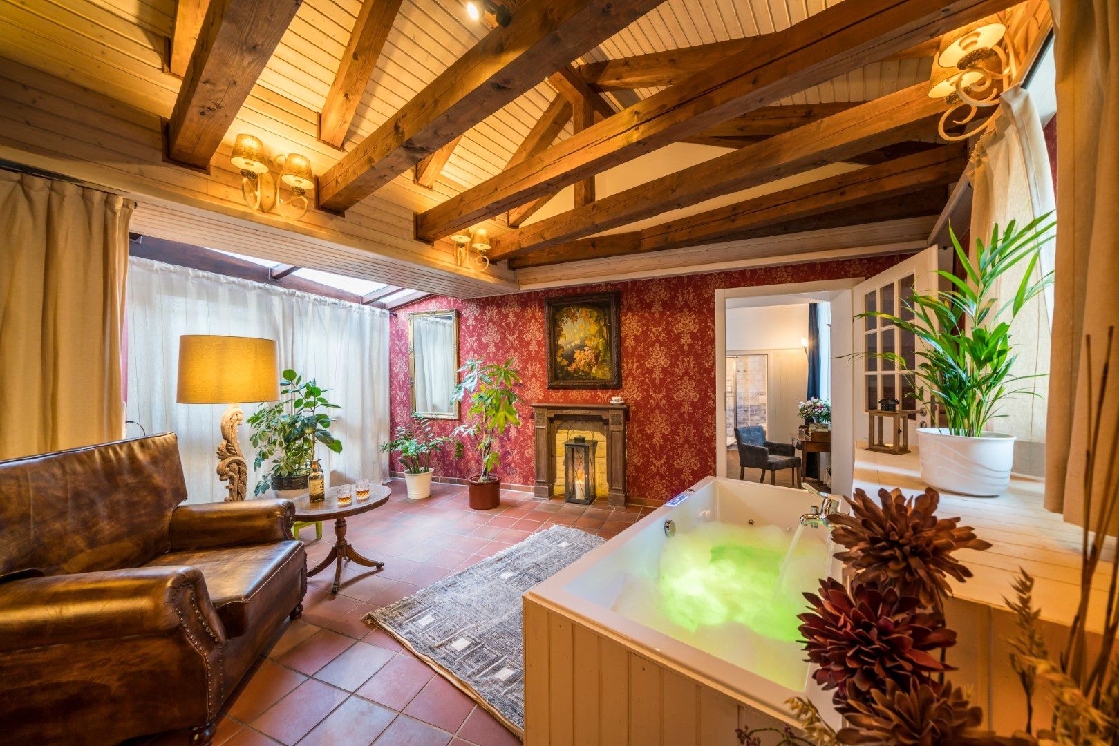 Gemütliches Zimmer mit freiliegenden Holzbalken, Ledersessel, Whirlpool mit grünem Wasser, Kamin und Pflanzen.