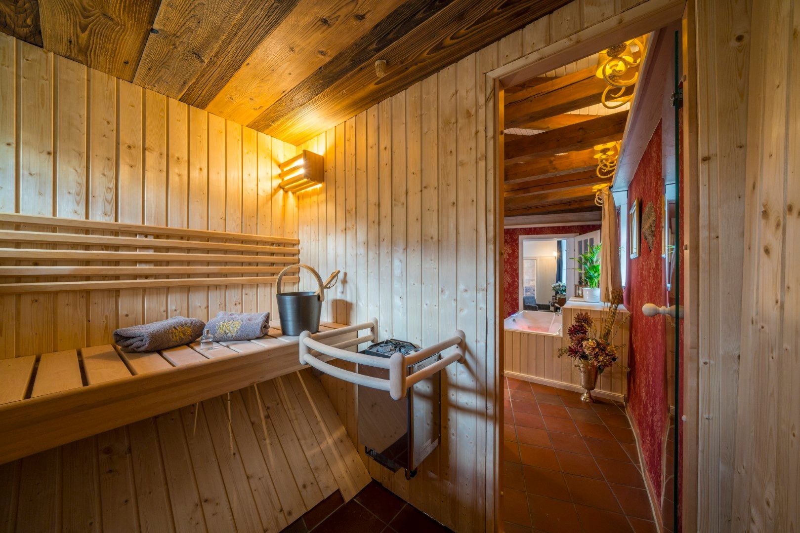 Saunainterieur aus Holz mit Bank, Eimer und Tür zu einem weiteren Raum.