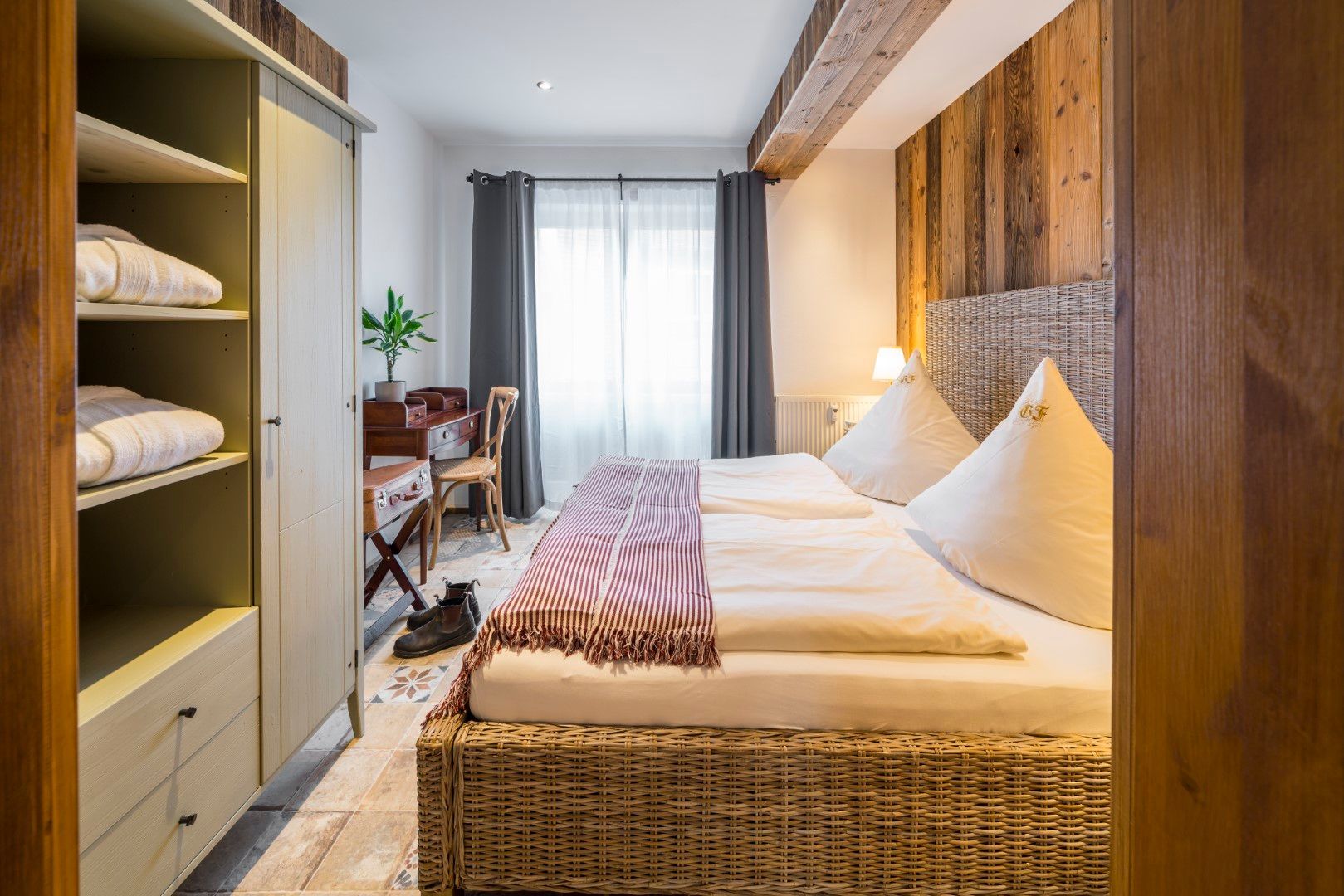 Schlafzimmer mit Korbbett, hölzernem Kopfteil und offenem Kleiderschrank.