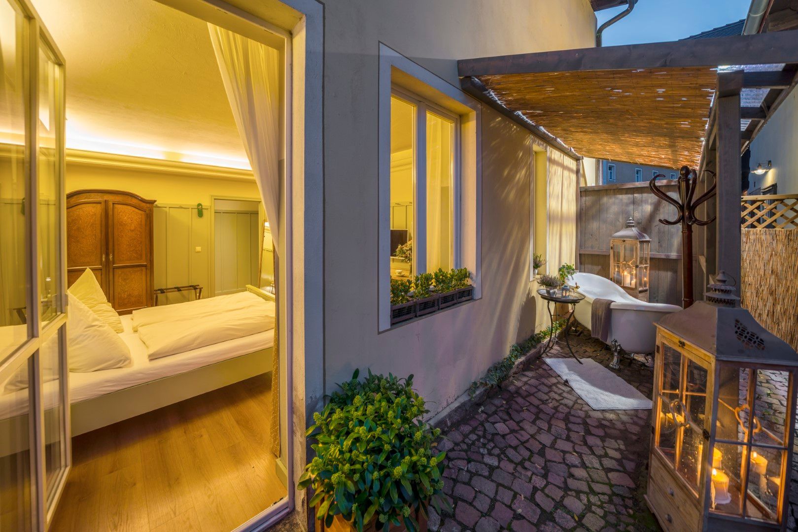 Schlafzimmer mit offener Tür zu einer Terrasse mit Außenbadewanne und Laterne.