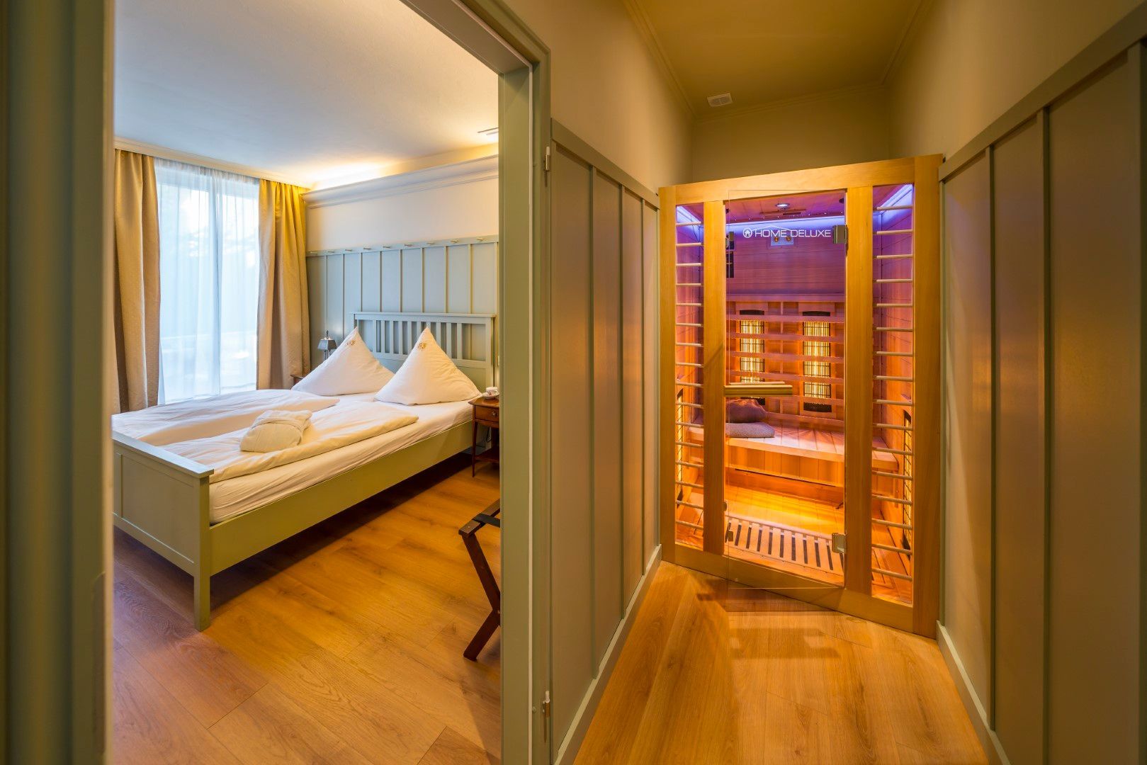 Schlafzimmertür mit Blick auf die Sauna. Grünes Schlafzimmer mit Bett und Holzboden. Die Saunatür ist offen.