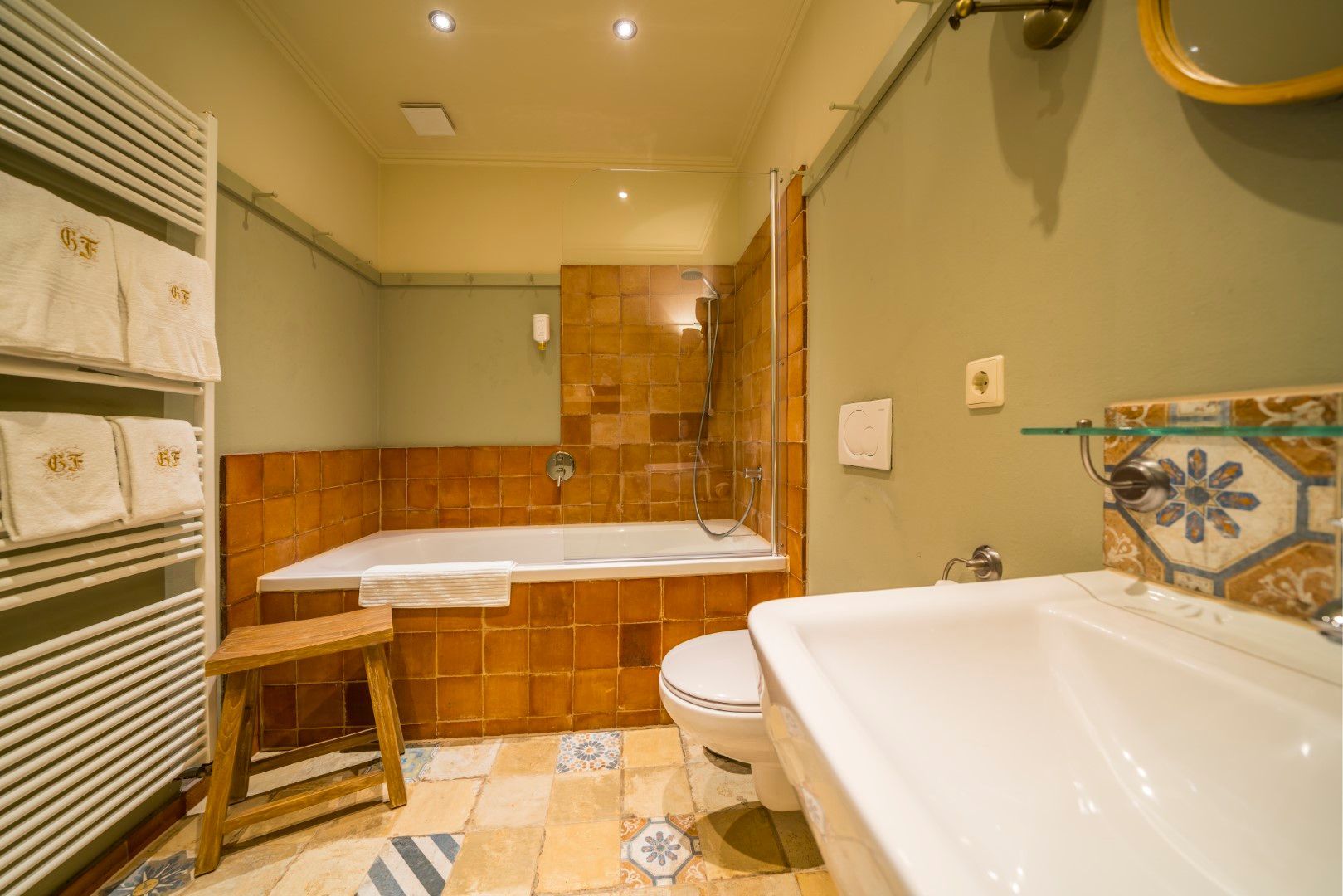 Badezimmer mit Badewanne, Waschbecken, Toilette sowie gefliesten Wänden und Boden. Farben: Beige, Orange und Blau.