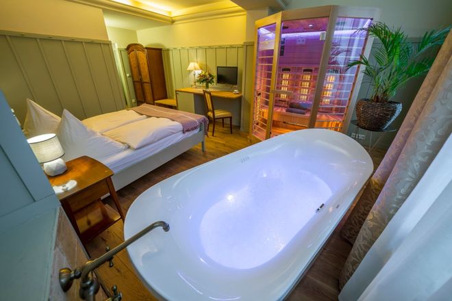 Schlafzimmer mit Badewanne, Sauna, Bett und Schreibtisch. Das Zimmer hat hellgrüne Wände und Holzboden.