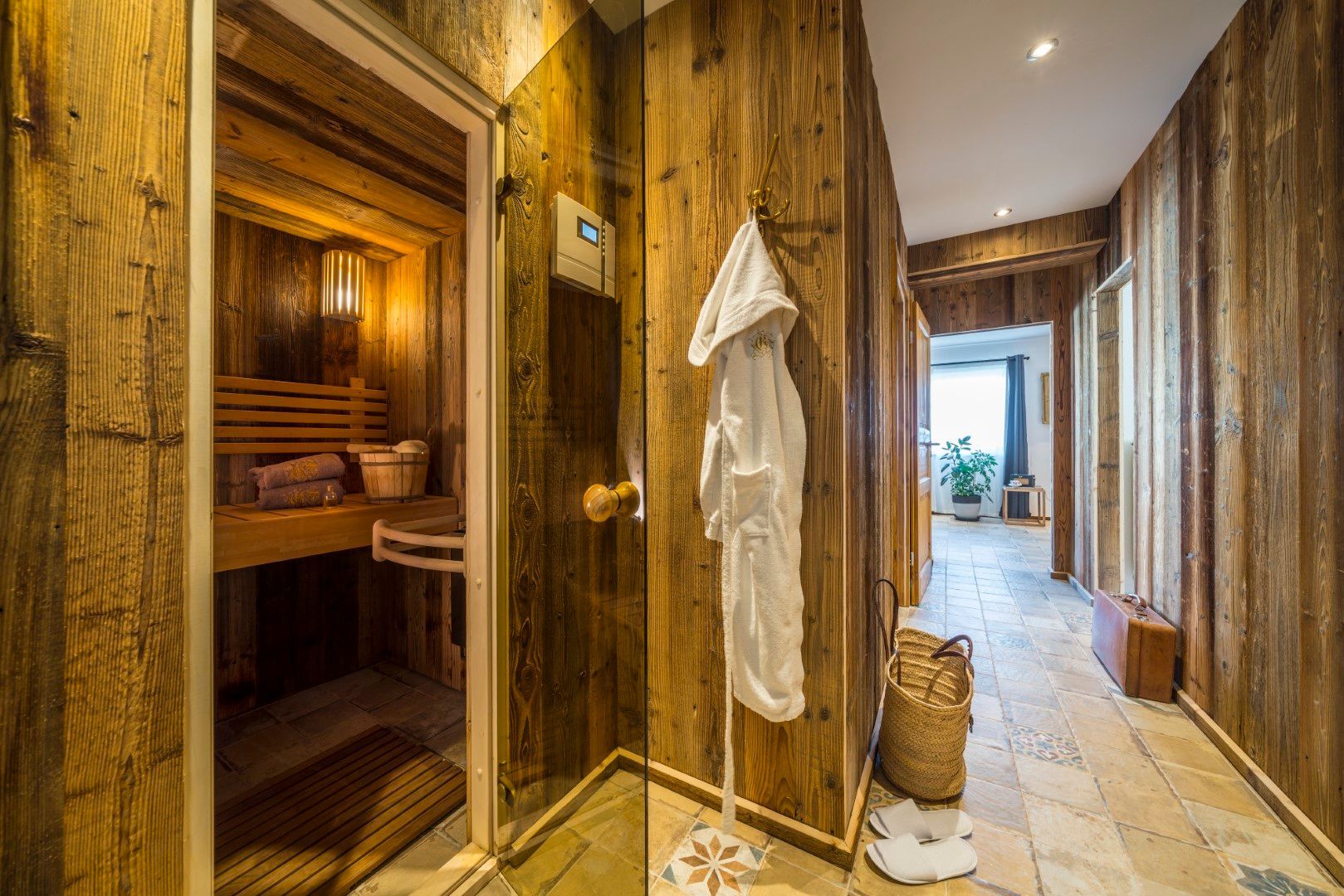 Holzsauna mit offener Tür, angrenzender Flur mit Bademantel, Korb und Koffer.