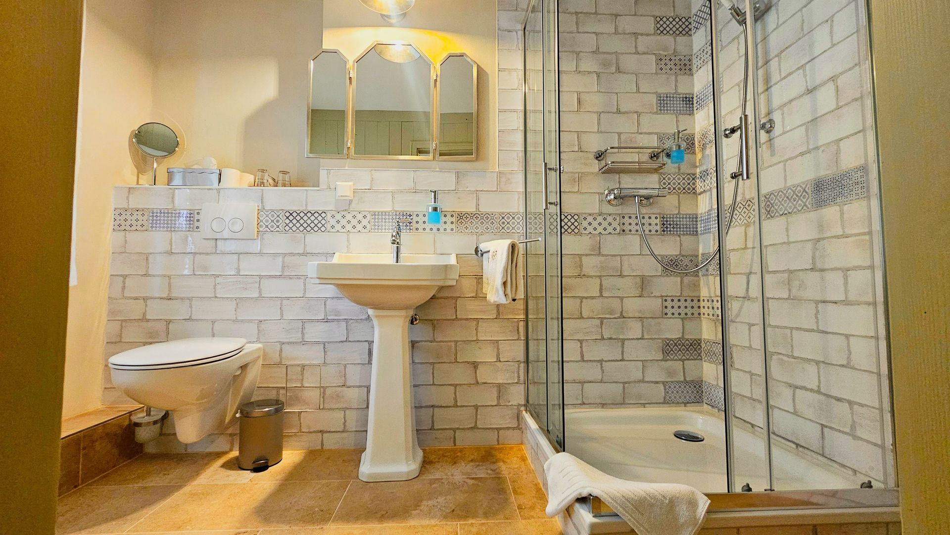 Badezimmer mit weißen Fliesenwänden, Standwaschbecken, Toilette und Duschkabine aus Glas.