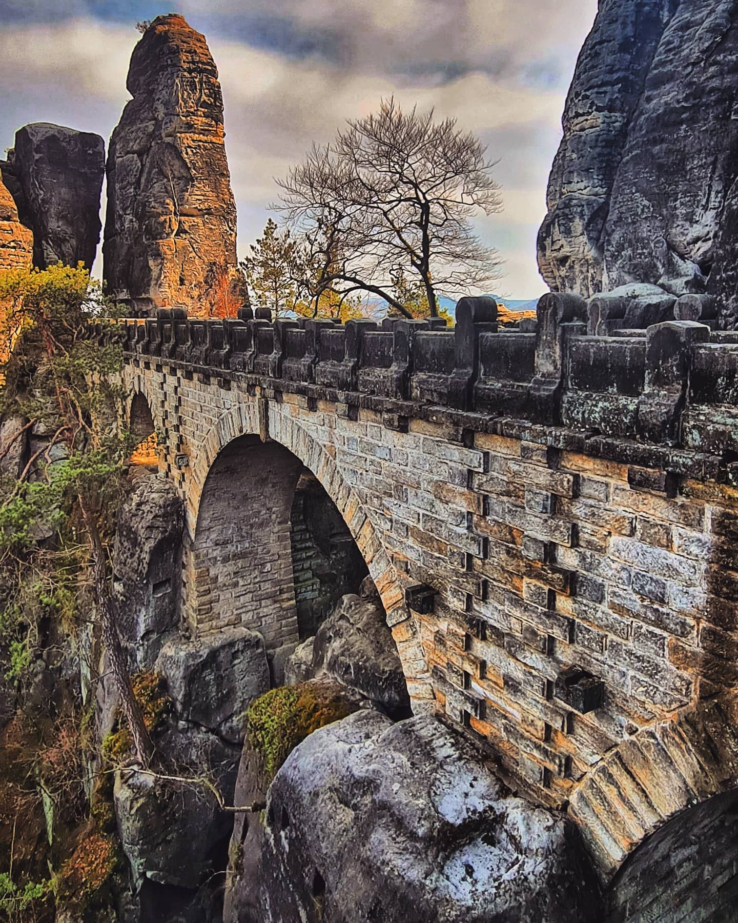 Steinbrückenbögen überspannen eine felsige Schlucht mit Sandsteinformationen. Bewölkter Himmel.