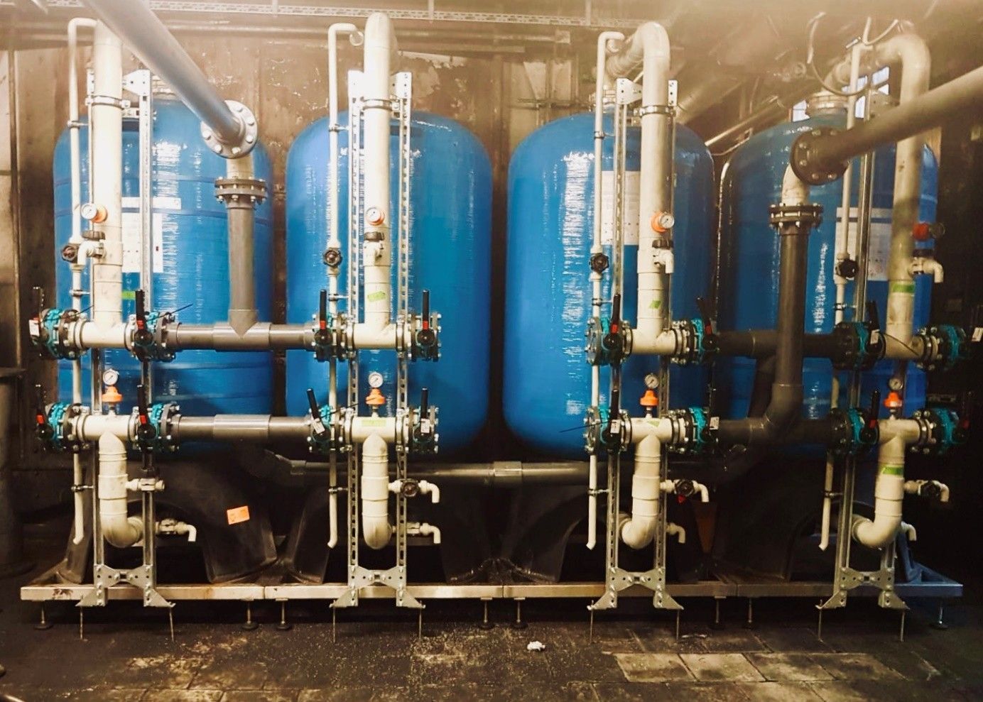 Drei metallische Industrietanks mit komplexen Rohrleitungen und Ventilen, montiert auf Metallrahmen.