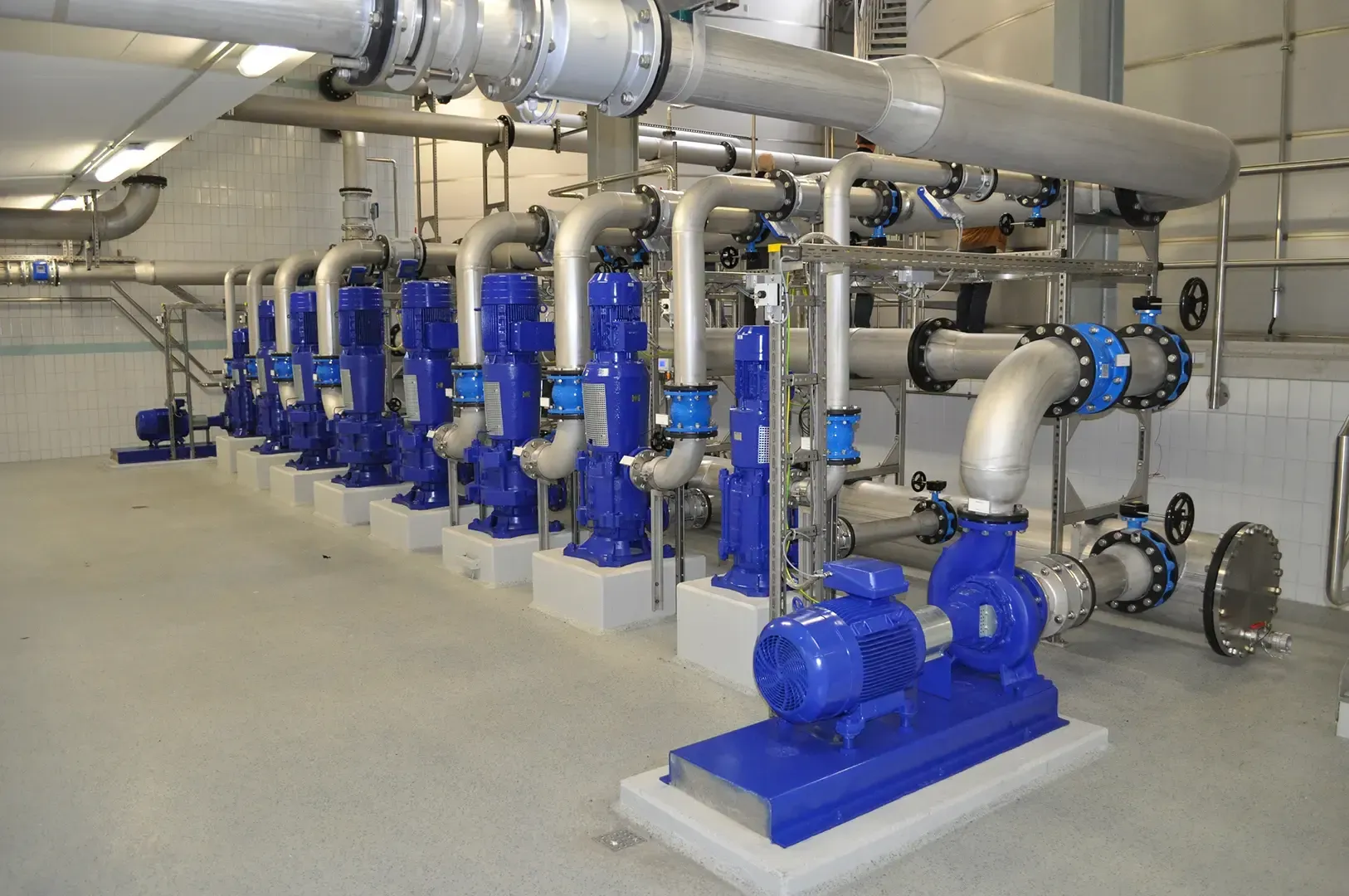 Zwei große weiße Industrietanks mit grünen und violetten Rohrleitungen in einer Anlage.