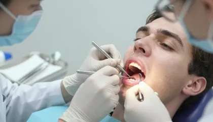 Primer plano de una persona sonriente con pecas en la cara y la mano apoyada cerca de la barbilla, con los ojos cerrados.