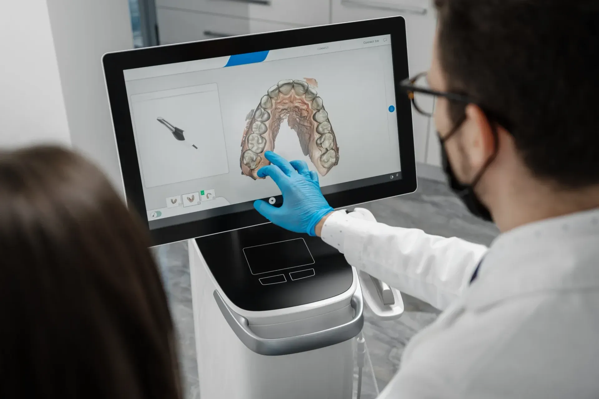 Un dentista señala una tomografía dental en 3D en la pantalla de una computadora mientras atiende