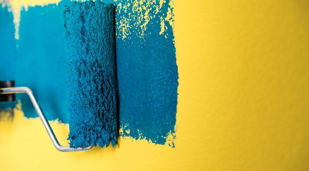 Un rodillo de pintura azul está pintando una pared amarilla.