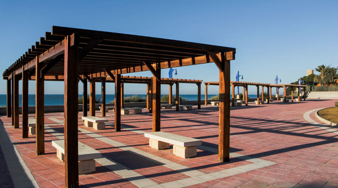 Una pérgola de madera se encuentra encima de una pasarela de ladrillos al lado del océano.