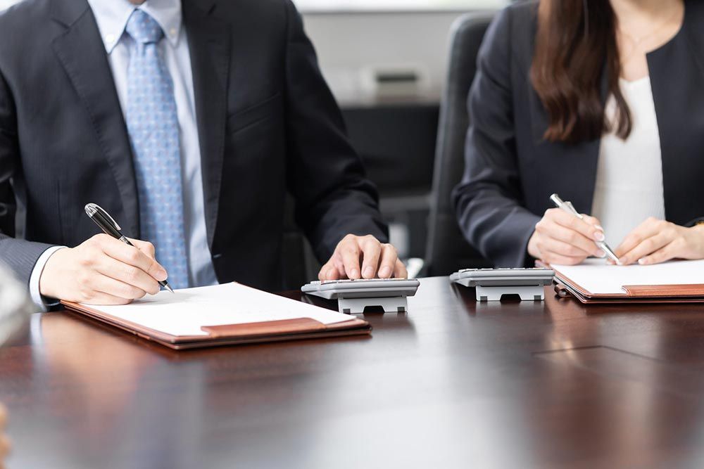 Dos personas vestidas de traje tomando notas en una mesa de conferencias durante una reunión.