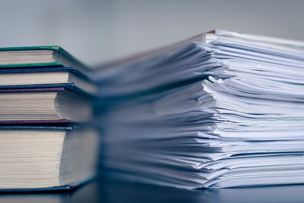 Montones de libros junto a una gruesa pila de papeles sobre un escritorio.