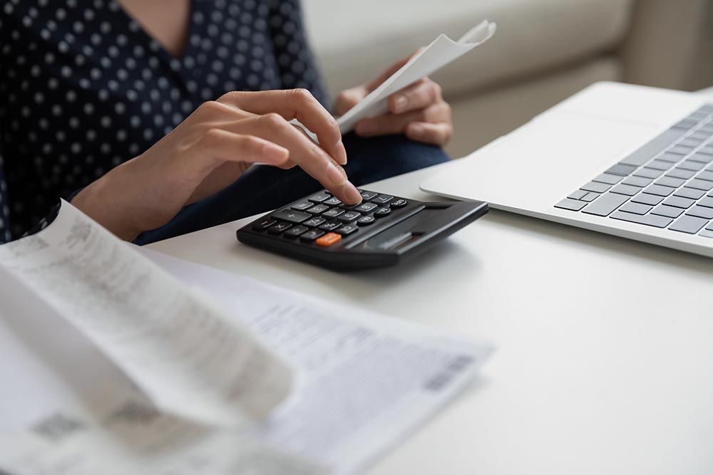 Manos usando una calculadora junto a una computadora portátil y papeles sobre un escritorio.