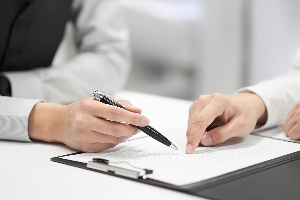 Dos personas revisan y firman un documento en un escritorio con un bolígrafo y un portapapeles.