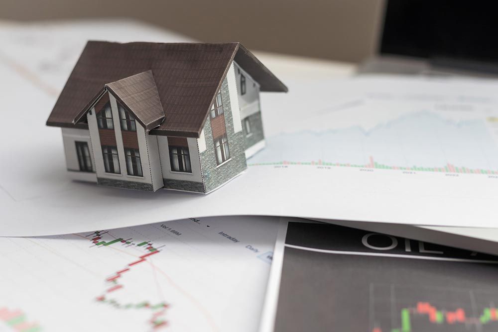 Modelo de casa en miniatura sobre gráficos financieros, que sugiere un análisis de inversión inmobiliaria.