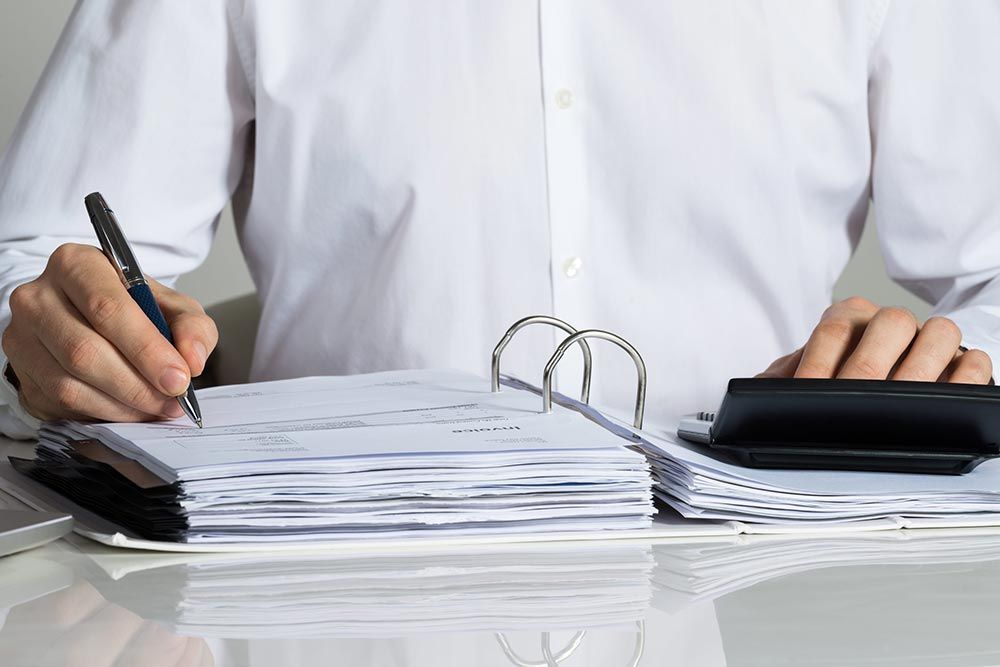 Persona escribiendo junto a una carpeta de anillas abierta y una calculadora sobre un escritorio.
